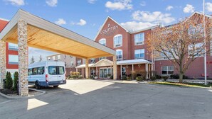 A Country Inn & Suites with a covered parking area, a brick building, and a van parked outside.
