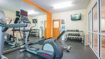 Ein Fitnessstudio mit Cardiogeräten, Kurzhanteln und einem Fernseher an der Wand.