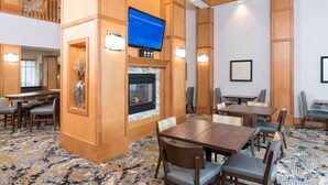 A hotel room with a fireplace, a flat-screen TV, and a dining area with tables and chairs. - Homewood Suites by Hilton Indianapolis-Airport/Plainfield (Plainfield)