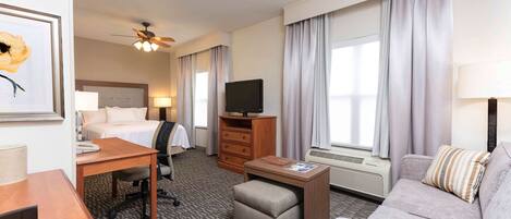 Habitación de hotel con cama, escritorio, silla, televisión, sofá y una mesita.