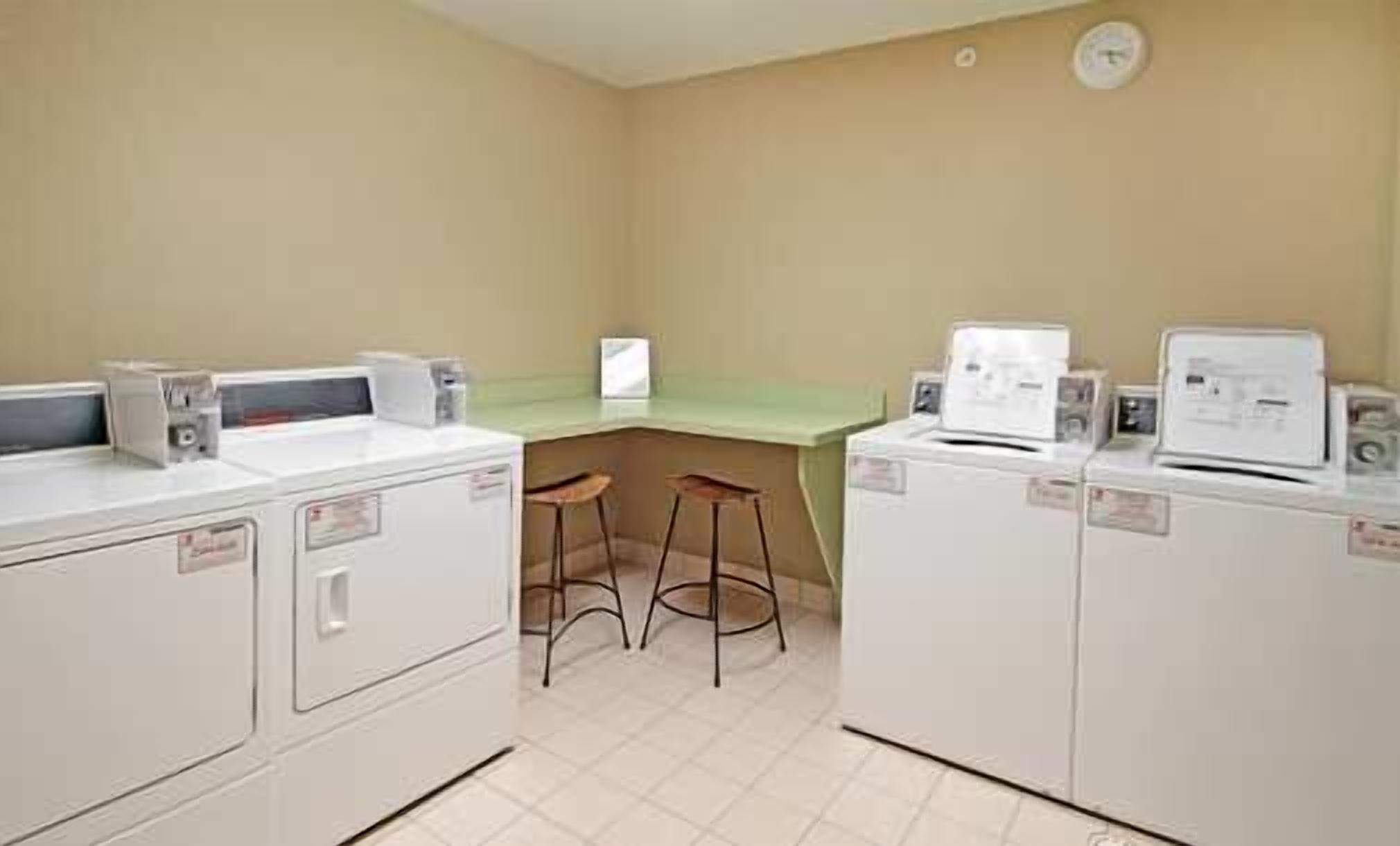 A laundry room with two washing machines, a countertop, and two stools.