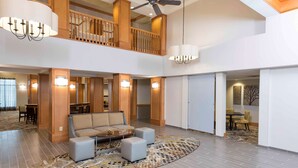 A spacious lobby with a high ceiling, a central seating area with a sofa and ottomans, a patterned rug, and a staircase leading to an upper level. - Homewood Suites by Hilton Indianapolis-Airport/Plainfield (Plainfield)