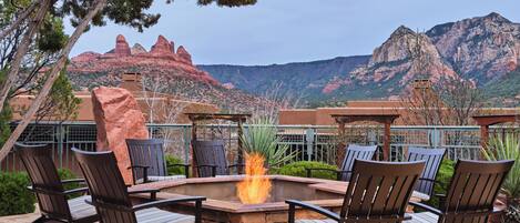 A fire pit surrounded by chairs, with a mountainous backdrop.