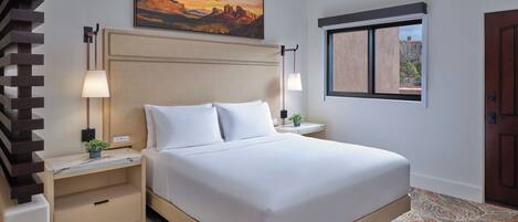 Ein Hotelzimmer mit Bett, Nachttischen, einem Gemälde, einem Fenster und einer Tür.