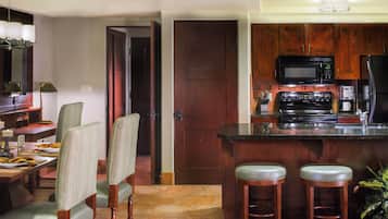 Una cocina con armarios de madera, un microondas, una estufa y un refrigerador. Hay dos taburetes de bar y una mesa de comedor con sillas.