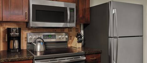 A kitchen with a stainless steel microwave, oven, and refrigerator, wooden cabinets, and a granite countertop.
