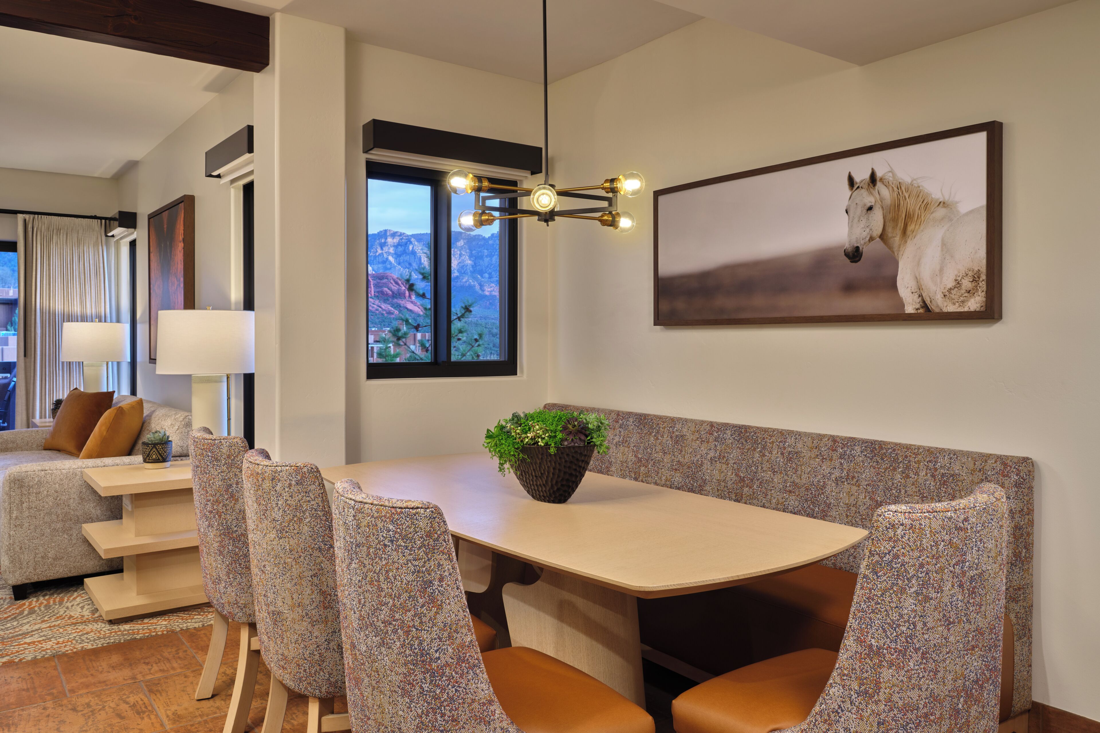 A dining area with a table, chairs, a plant, and a horse painting on the wall.