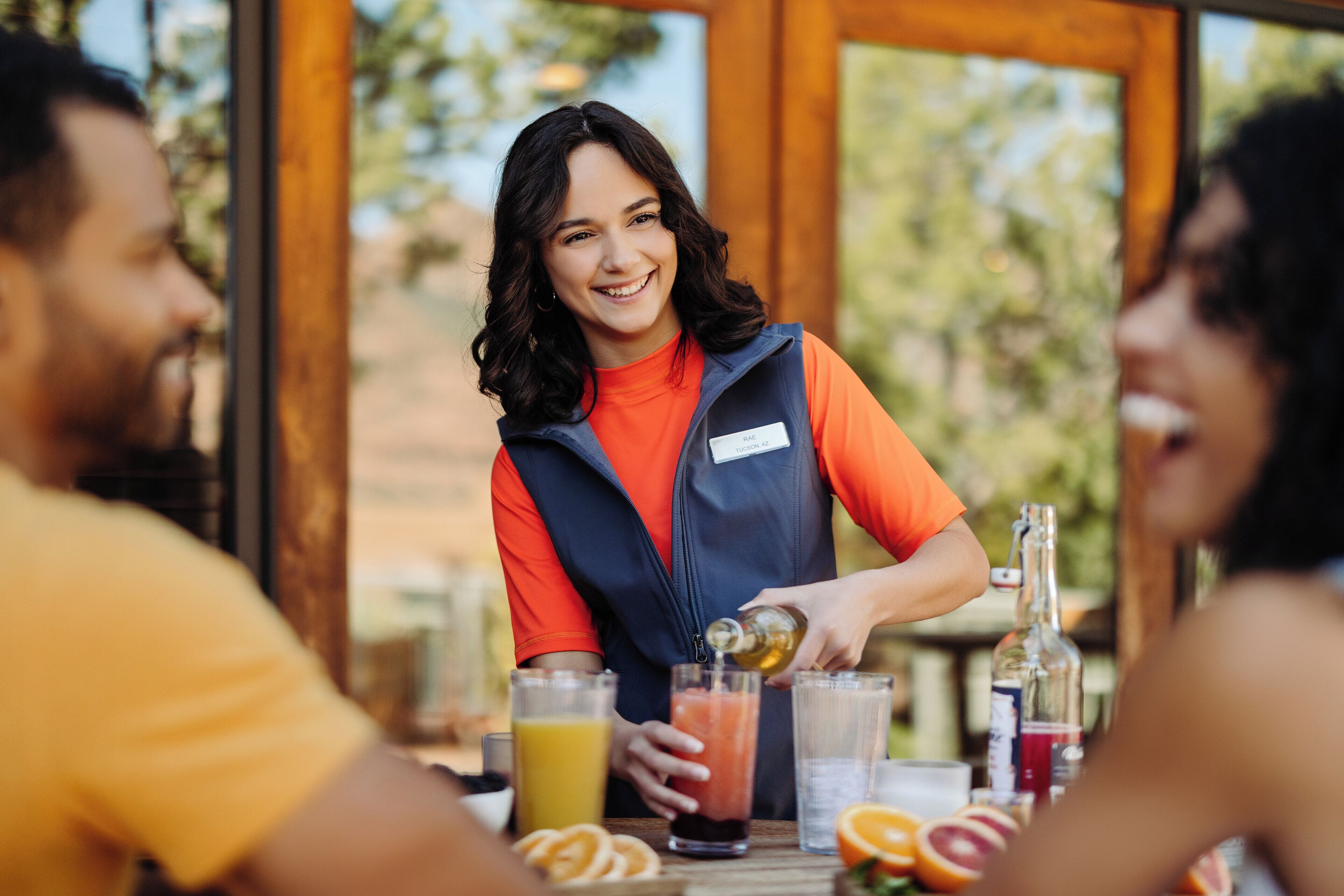 Une personne verse une boisson dans un verre, à une table où se trouvent diverses boissons et des fruits.