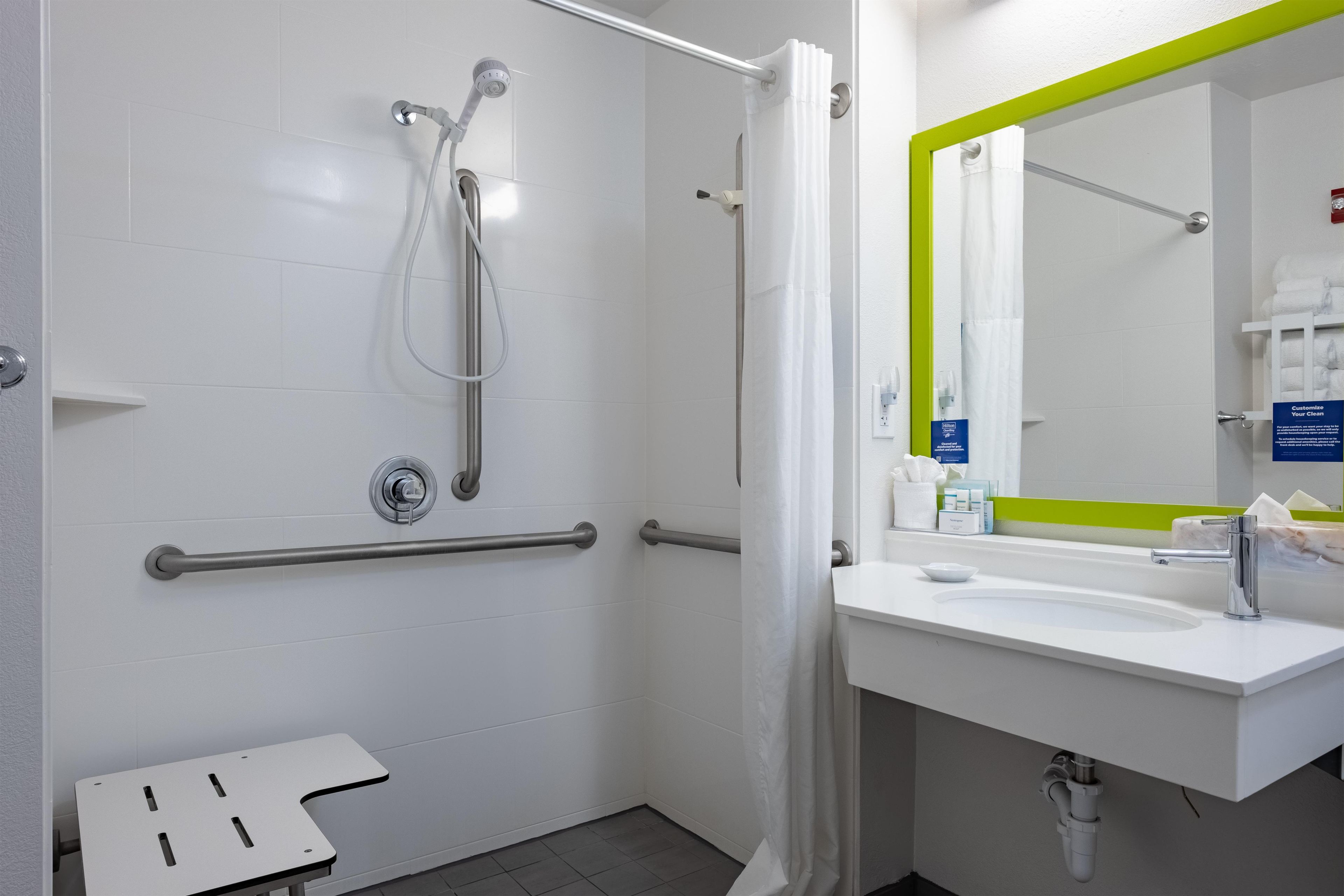 A modern bathroom with a shower, grab bars, a sink, and a mirror.