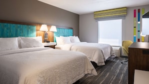Une chambre d’hôtel avec deux lits, un bureau, une chaise et une grande fenêtre.