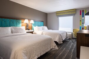 Quarto de hotel com duas camas, uma escrivaninha, uma cadeira e uma janela com vista.