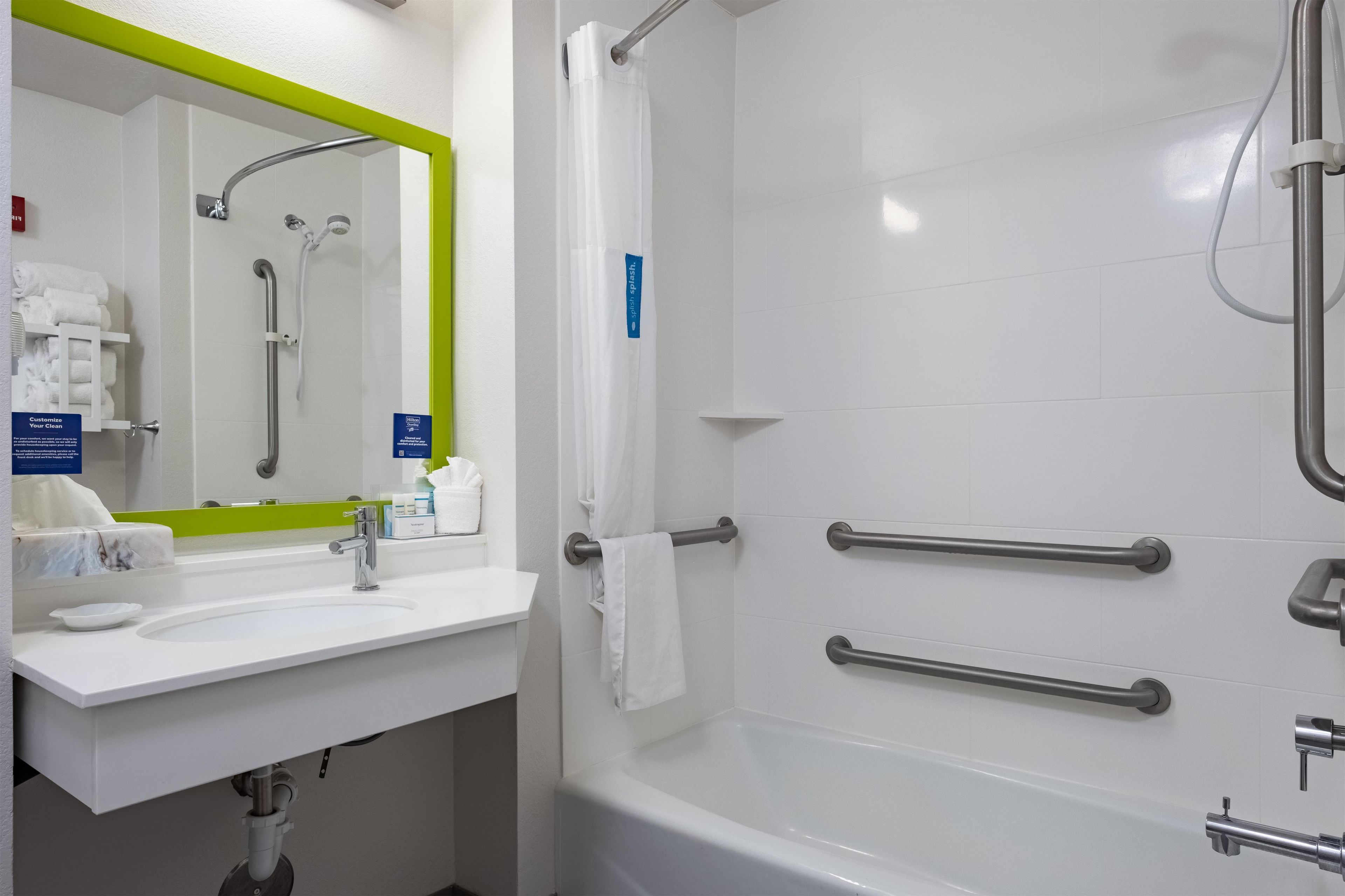 A bathroom with a white sink, mirror, and bathtub. There are handrails on the bathtub and a towel rack.
