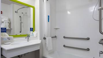 A bathroom with a white sink, mirror, and bathtub. There are handrails on the bathtub and a towel rack.