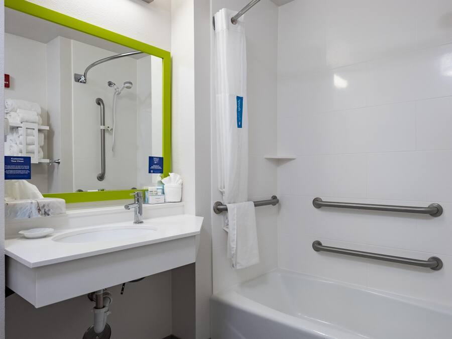 A bathroom with a white sink, mirror, and bathtub. There are handrails on the bathtub and a towel rack.