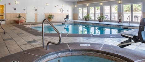 An indoor swimming pool with a hot tub, tiled flooring, and potted plants.