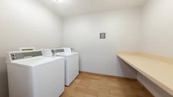 A laundry room with a front-loading washer and dryer, a small shelf, and a sign indicating the availability of laundry products and vending machines.
