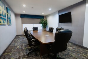 Un salón de conferencias con una larga mesa, seis sillas, una planta en maceta, un televisor de pantalla plana y obras de arte en las paredes.
