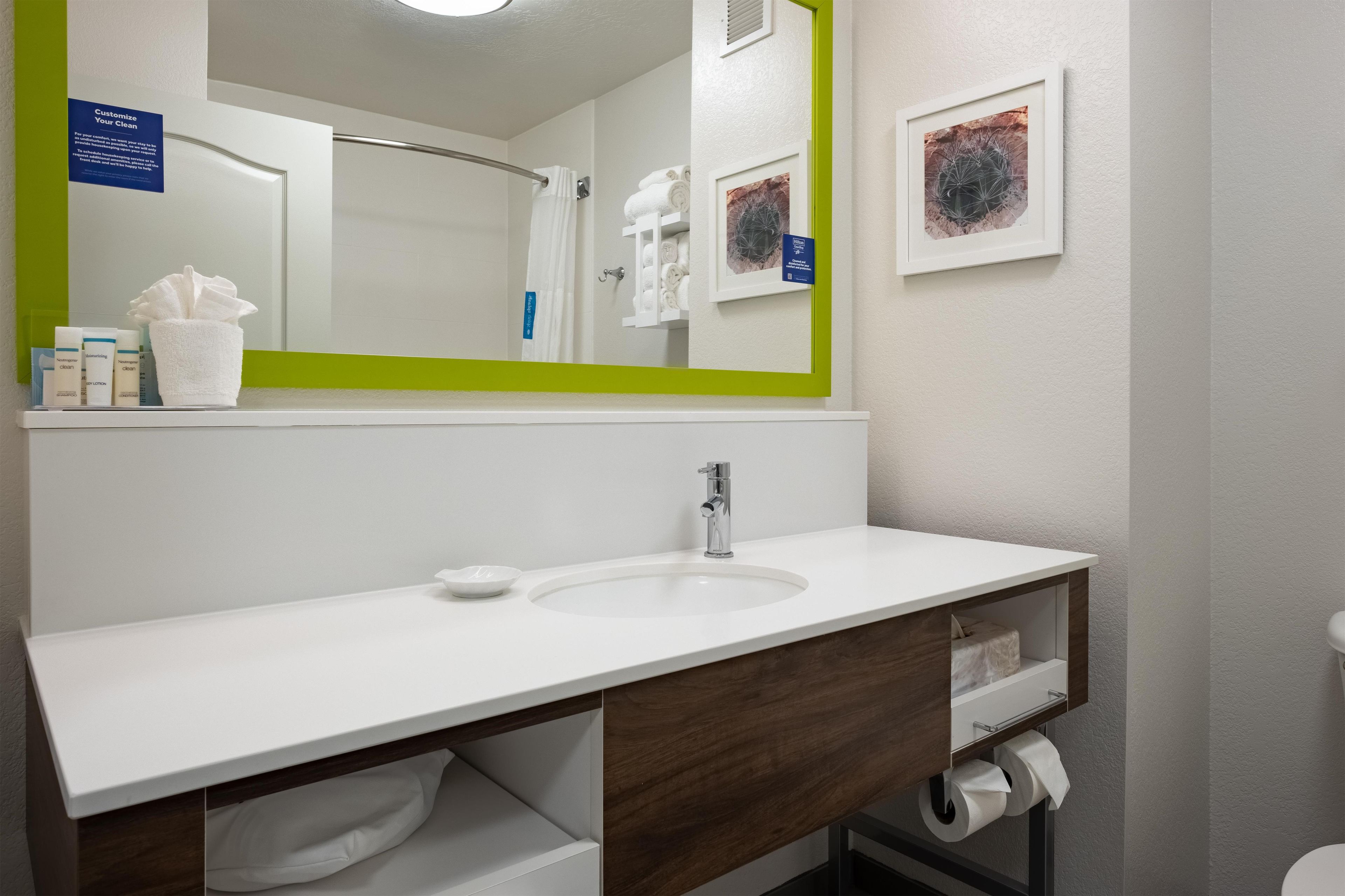 A bathroom with a white sink, a mirror with a green frame, a towel rack, and a framed picture on the wall.