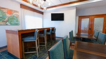 Un comedor de hotel con bar, asientos y un televisor de pantalla plana.