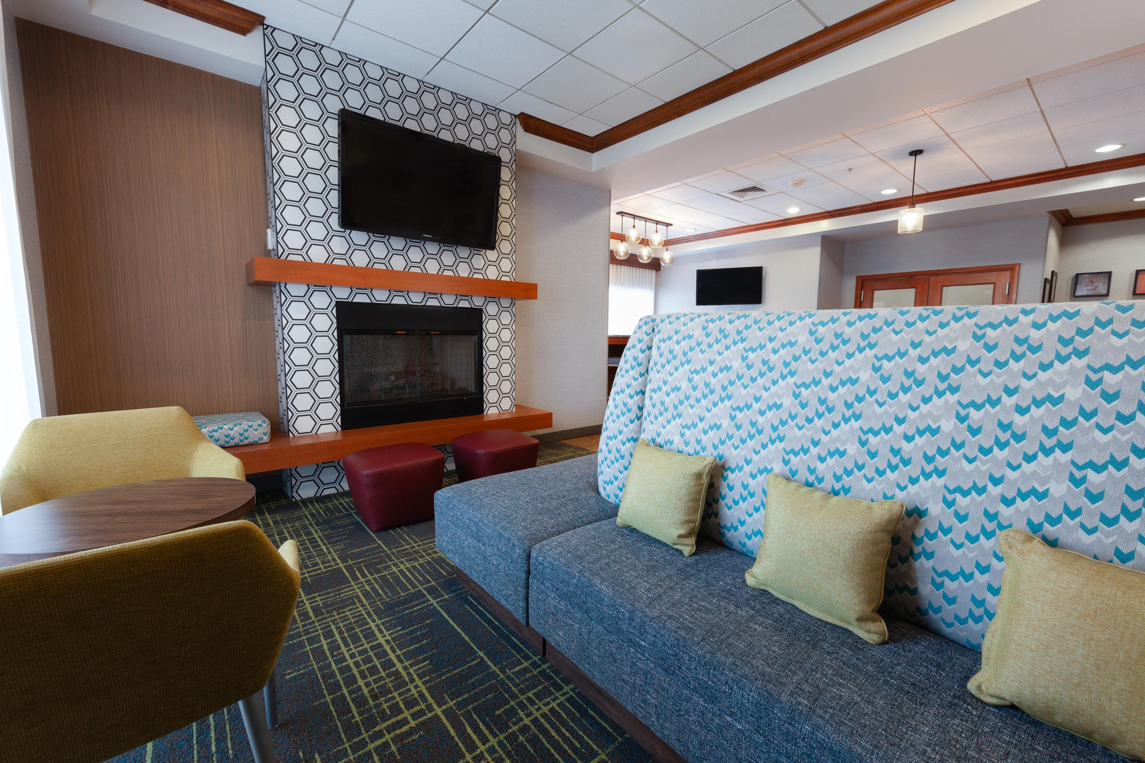 A hotel room with a sofa, chairs, a small table, a fireplace, and a TV mounted on the wall.