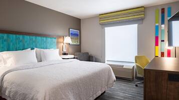 A hotel room with a large bed, a desk, a chair, a window, and a wall-mounted air conditioner.