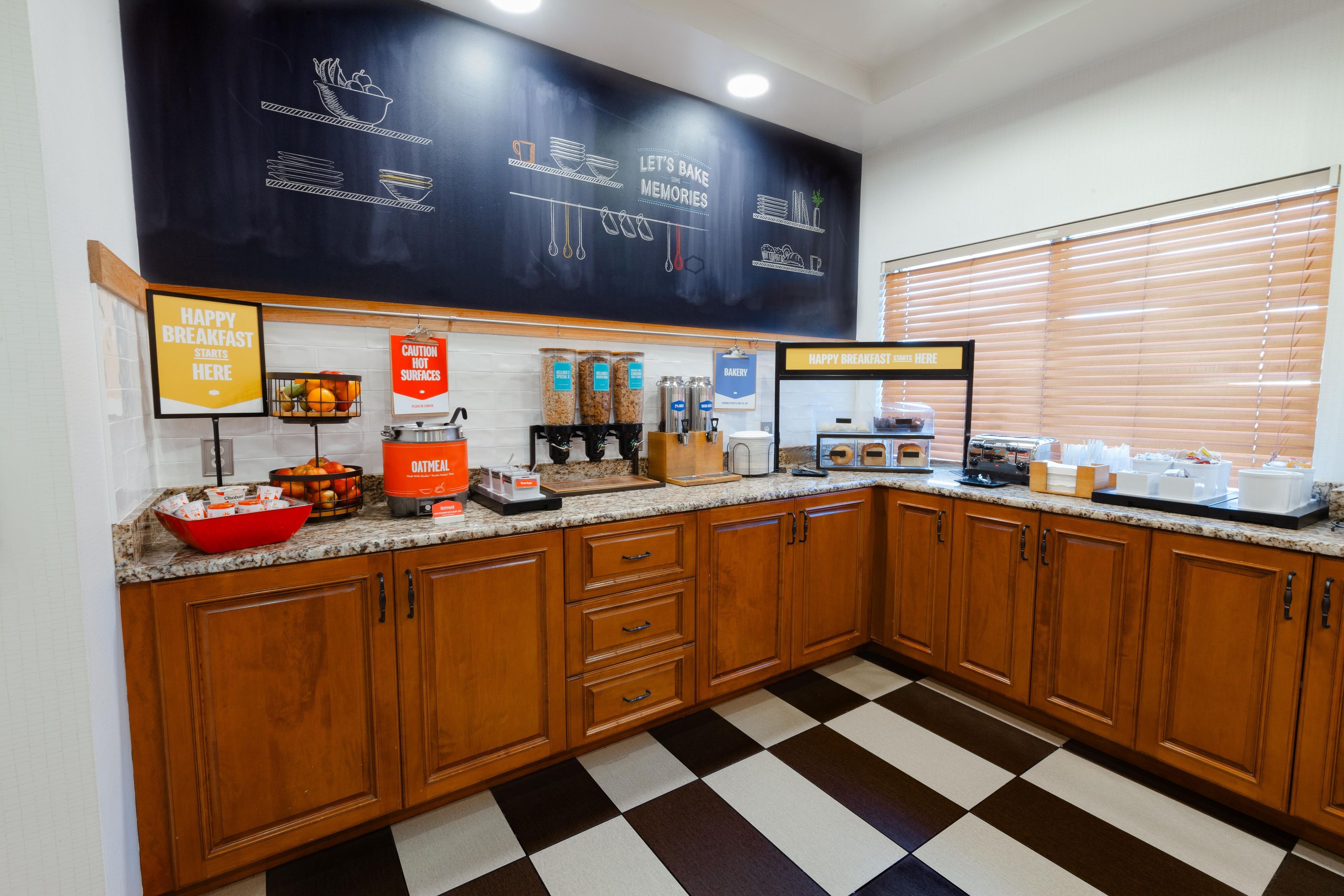 A breakfast bar with a chalkboard menu, a coffee machine, and a variety of food items.