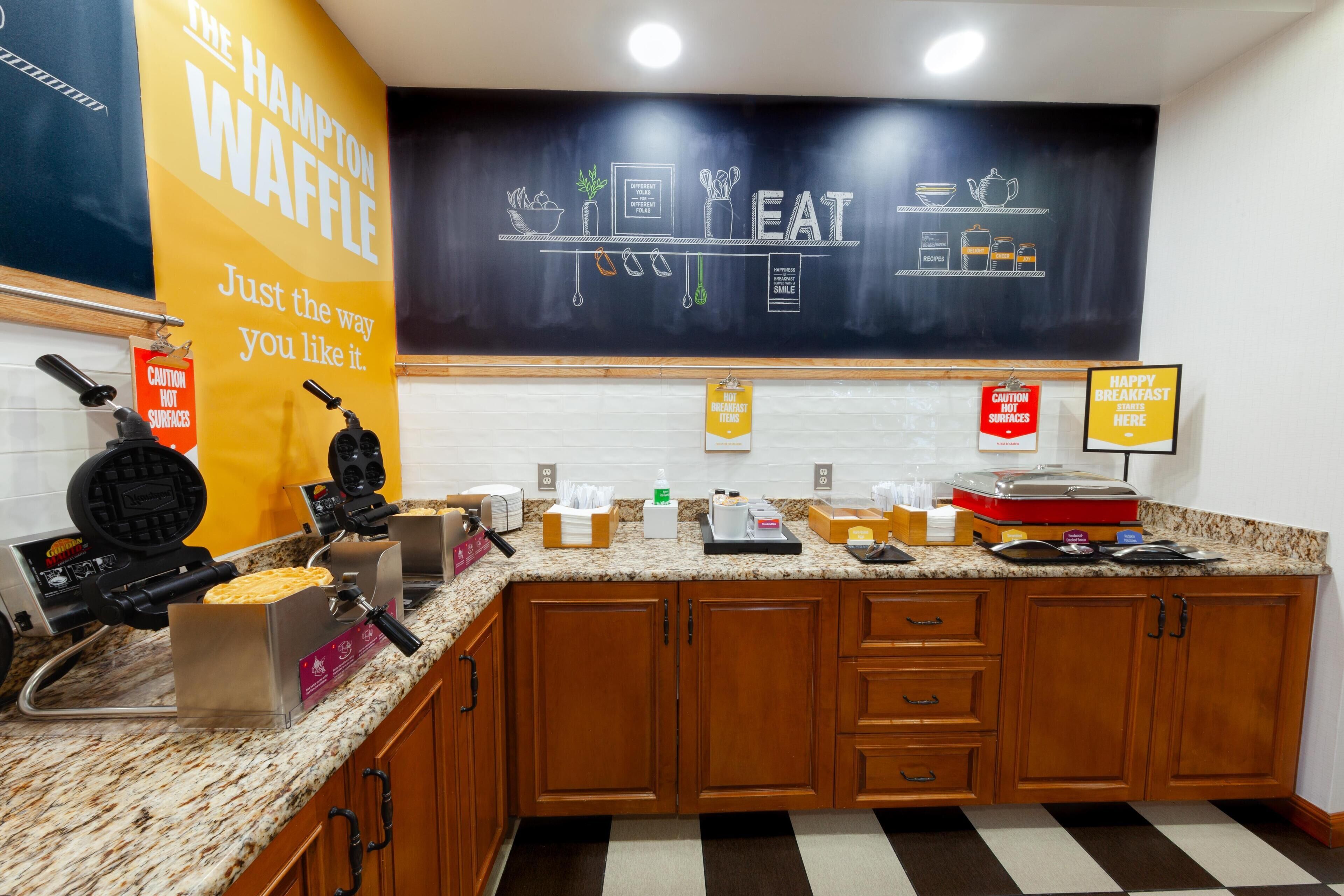 A kitchen with waffle makers, a chalkboard with food-related drawings, and various kitchen items on the counter.