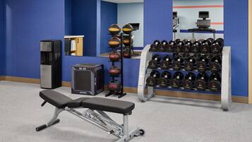 Gimnasio con equipo de ejercicio, incluyendo una banca, mancuernas y un dispensador de agua.