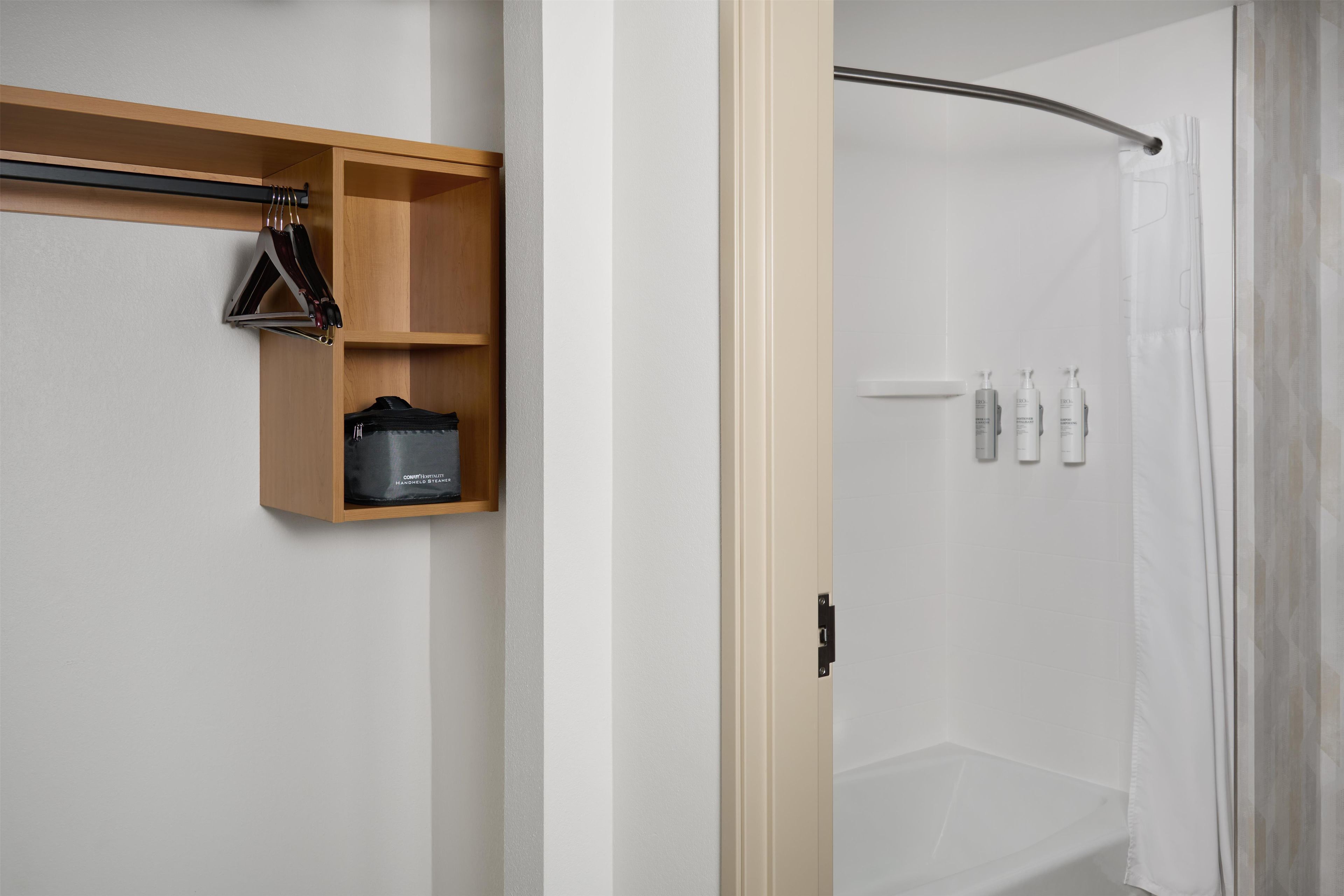 A bathroom with a shower, a wooden shelf with toiletries, and a black bag.