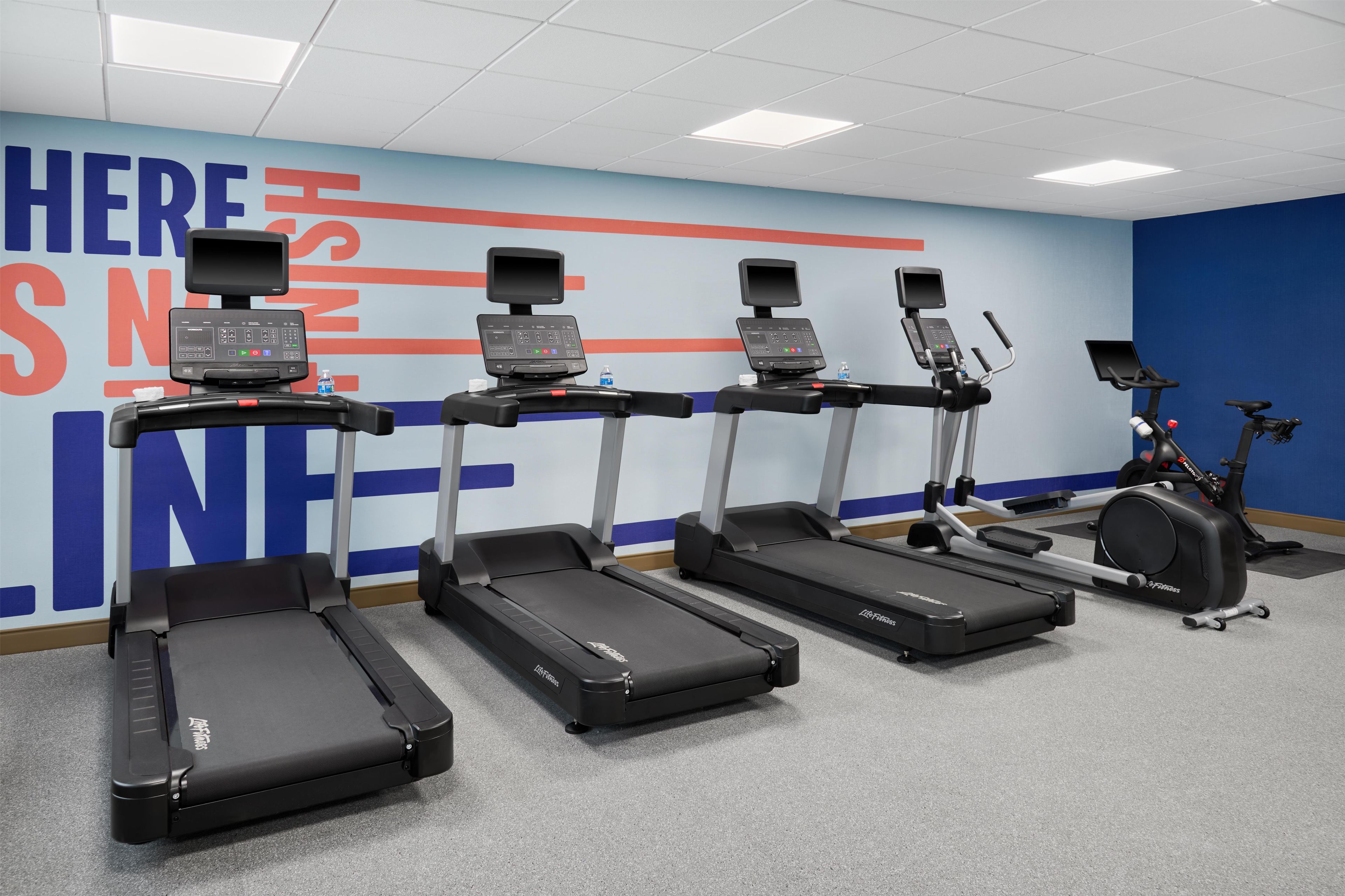 Un centre de remise en forme équipé de tapis de course, d’un vélo d’appartement et d’un mur orné de messages motivants.