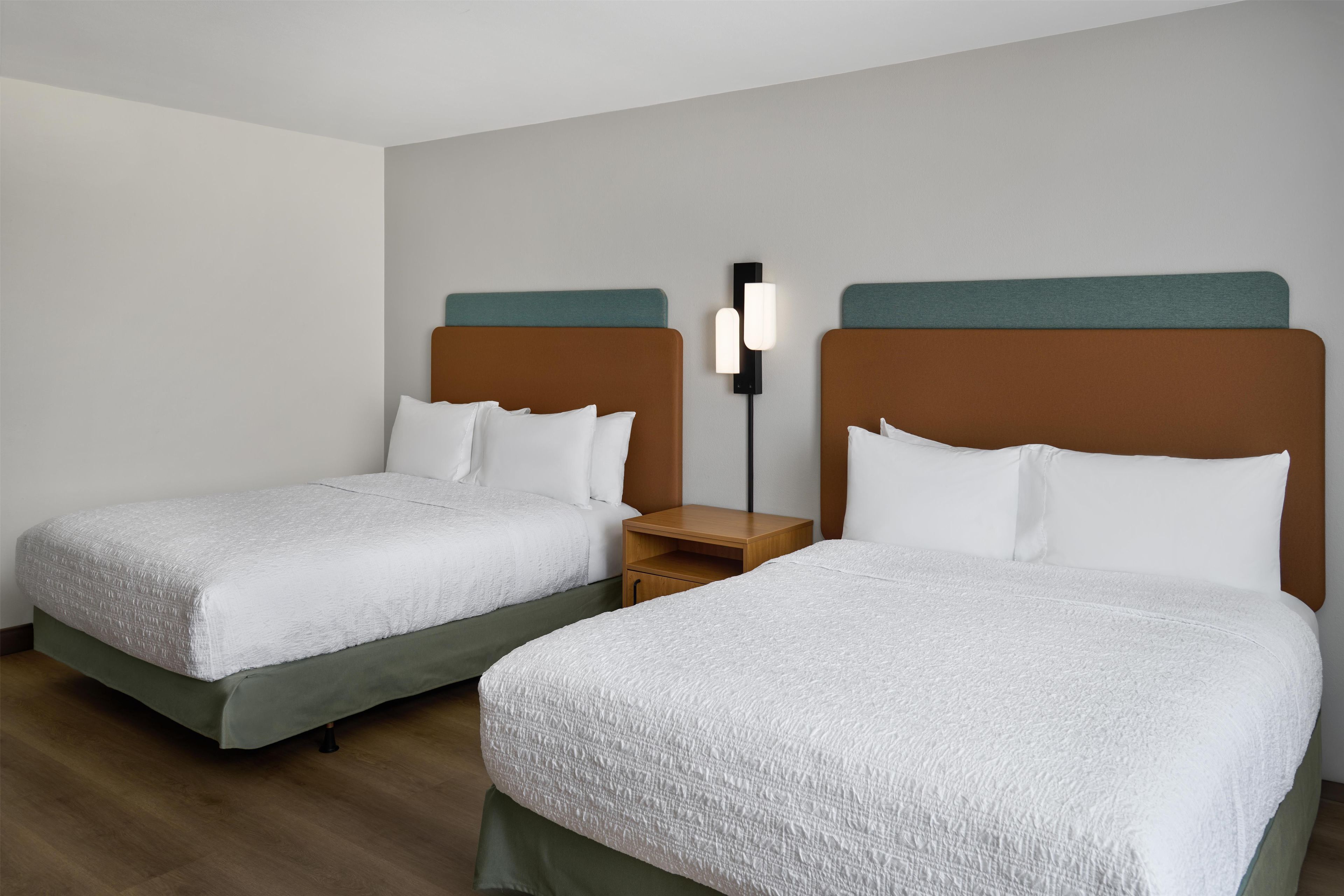 Una habitación de hotel con dos camas, cada una con cabecera, mesita de noche y lámpara de pared.