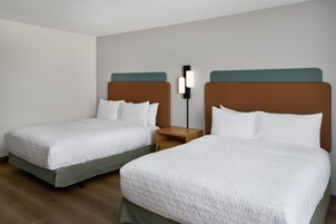 Una habitación de hotel con dos camas, cada una con cabecera, mesita de noche y lámpara de pared.
