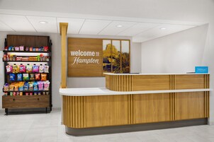 Una recepción con un letrero que dice 'welcome to Hampton', estantes con aperitivos y un letrero de Hilton Honors.