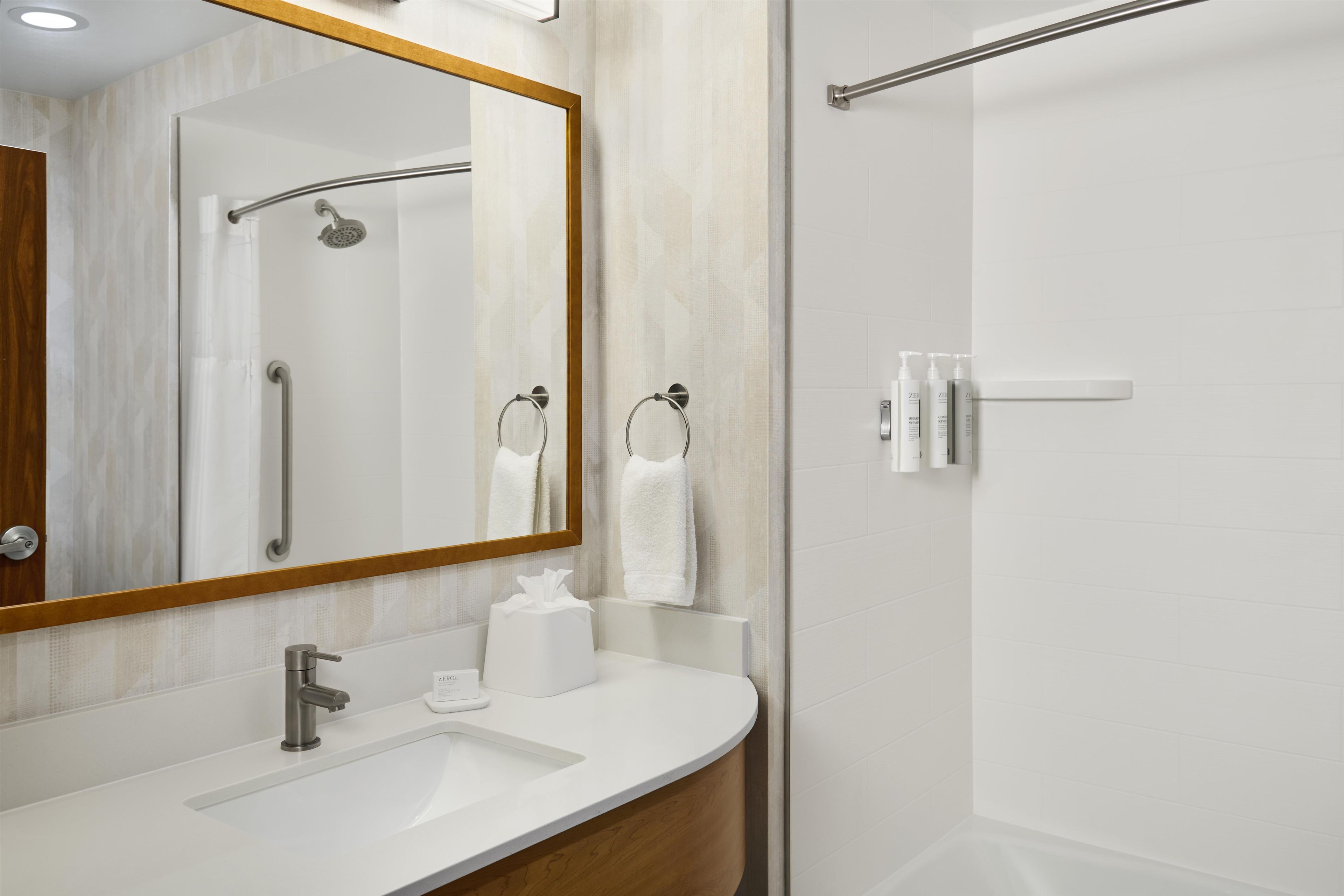 Une salle de bain moderne équipée d’un lavabo, d’un miroir, d’une douche et d’un porte-serviettes.