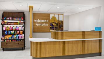 A reception desk with a 'welcome to Hampton' sign, snack shelves, and a Hilton Honors sign.