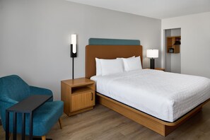A hotel room with a bed, a nightstand, a lamp, a chair, and a wooden side table. - Hampton Inn by Hilton Odessa (Odessa)