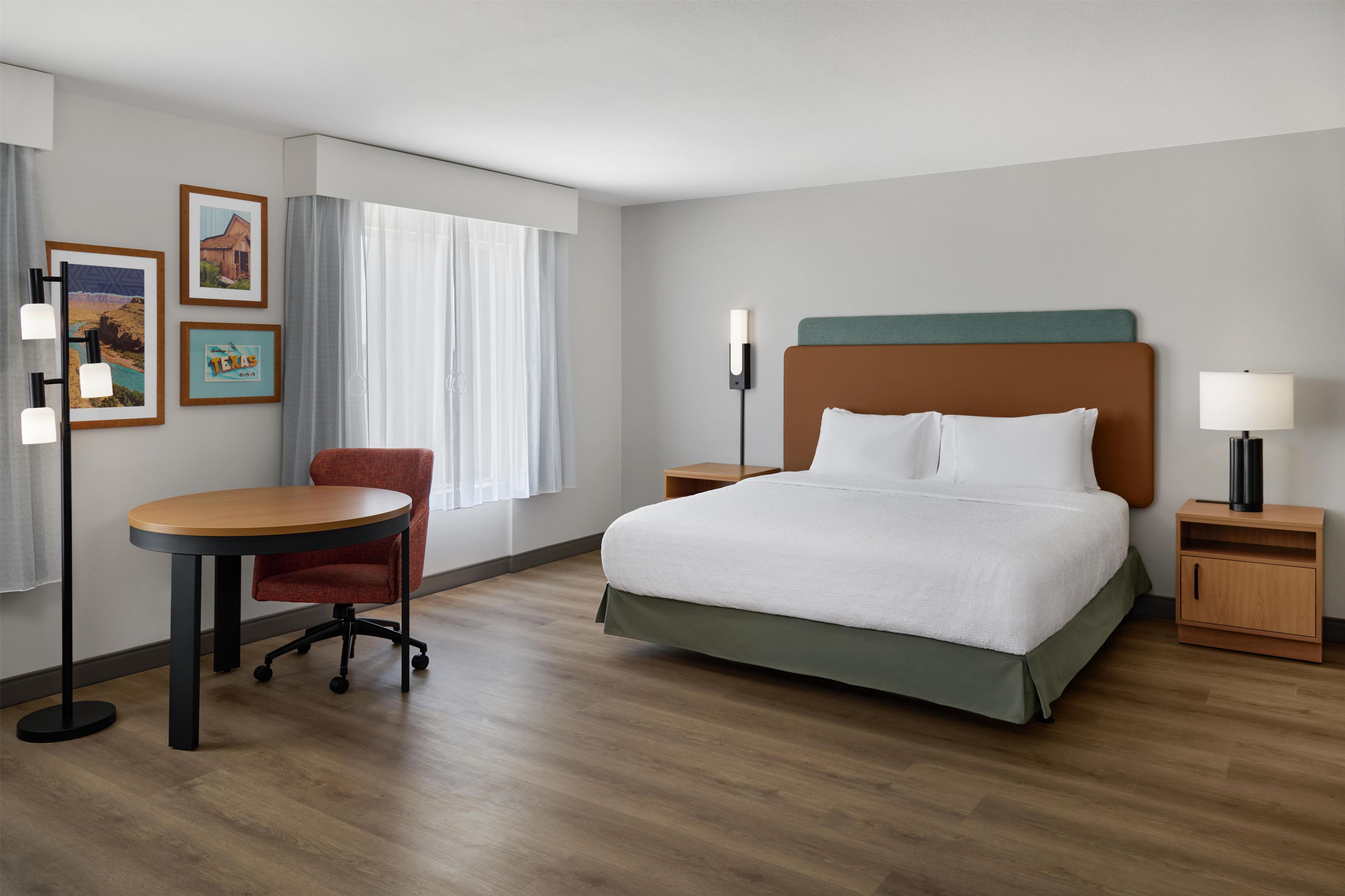 Una habitación de hotel con cama, escritorio, silla, mesita de noche y lámpara.