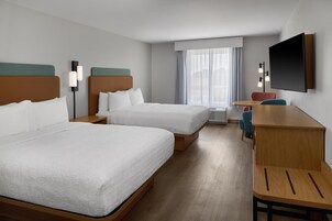 Habitación de hotel con dos camas, un escritorio, una silla, un televisor y una ventana con cortinas.