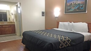 A hotel room with a bed, a nightstand, a framed picture on the wall, and a bathroom visible through an open door. - Americas Best Value Inn Beaumont, CA (Beaumont)