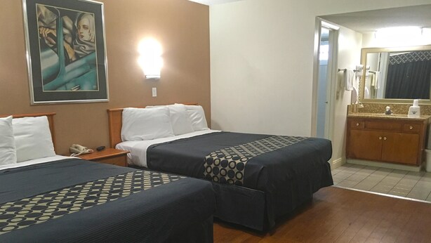 A hotel room with two beds, a nightstand with a phone, a painting on the wall, a bathroom with a mirror and sink. - Americas Best Value Inn Beaumont, CA (Beaumont)