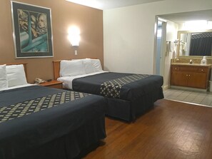 A hotel room with two beds, a nightstand with a phone, a painting on the wall, a bathroom with a mirror and sink. - Americas Best Value Inn Beaumont, CA (Beaumont)