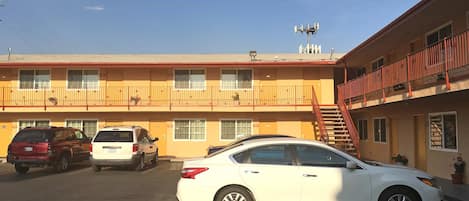 A multi-story motel with a red exterior, a parking lot with several cars, and a staircase leading to the upper floors.