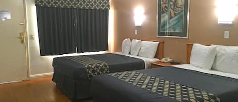 A hotel room with two beds, a door, a window with curtains, a painting on the wall, and a bedside table with a phone.