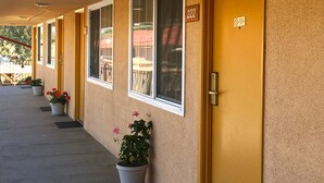 A row of hotel doors with a number sign, potted plants, and a balcony visible through the windows. - Americas Best Value Inn Beaumont, CA (Beaumont)
