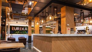 A modern bar area with a wooden counter, hanging pendant lights, and a visible bar stocked with bottles. - Yomo Eureka (Escaldes-Engordany)