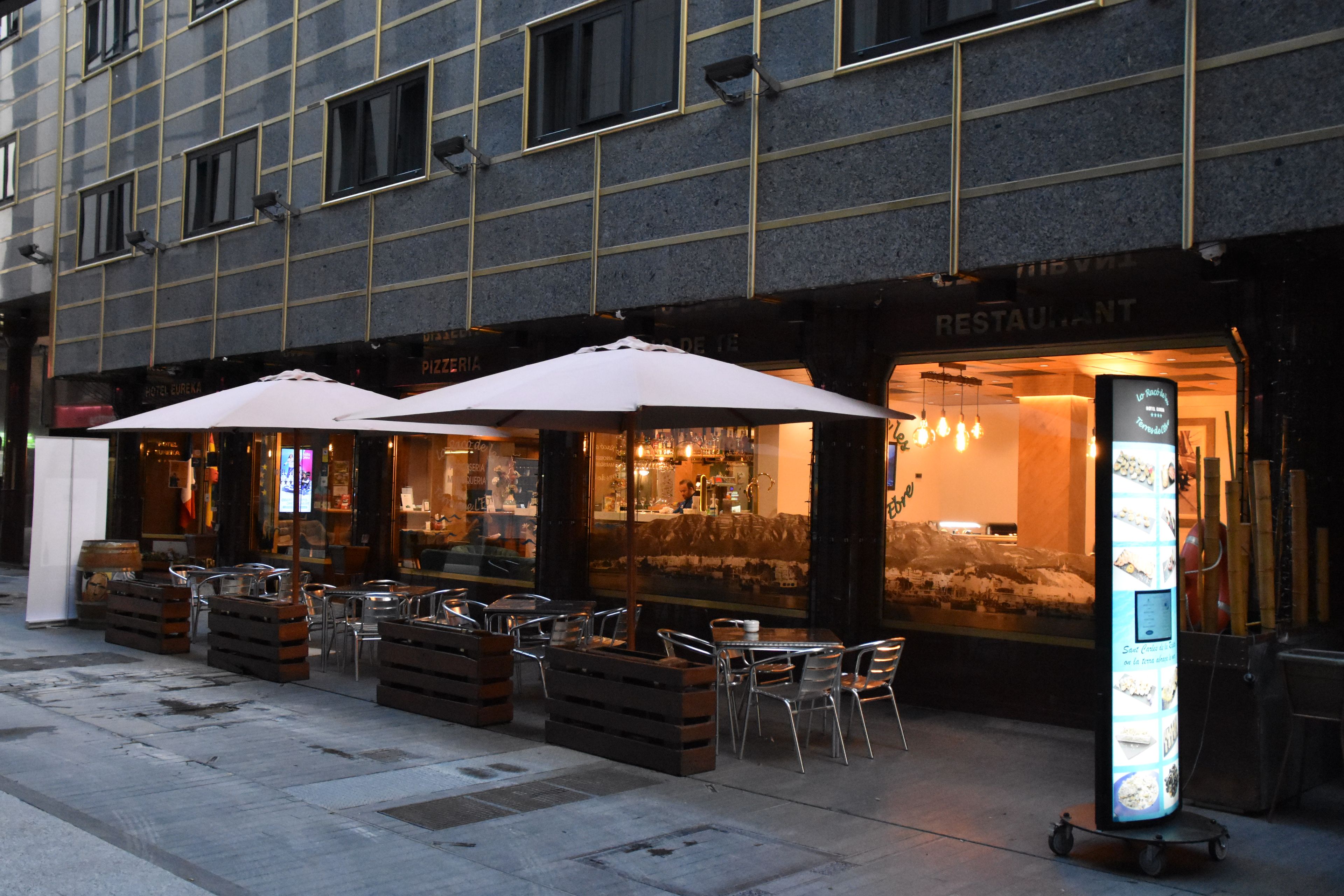 Un área de estar al aire libre con mesas y sillas, un edificio con el letrero de un restaurante y un menú digital.