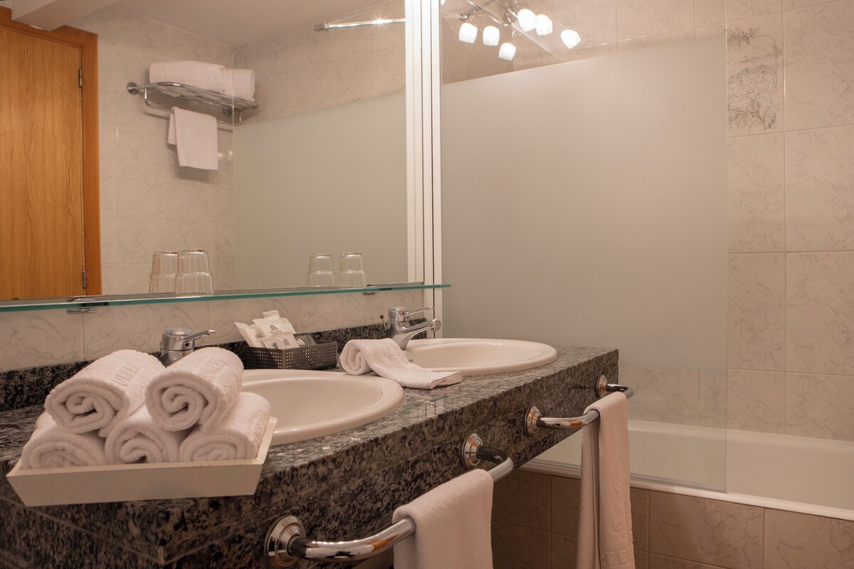 A bathroom with two sinks, a glass-topped vanity, a large mirror, and a bathtub.
