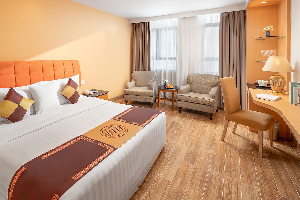 A hotel room with a large bed, two armchairs, a small table, and a desk with a lamp.