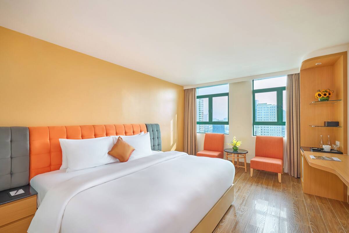 A hotel room with a large bed, a desk, a chair, and a small table with a vase of flowers.