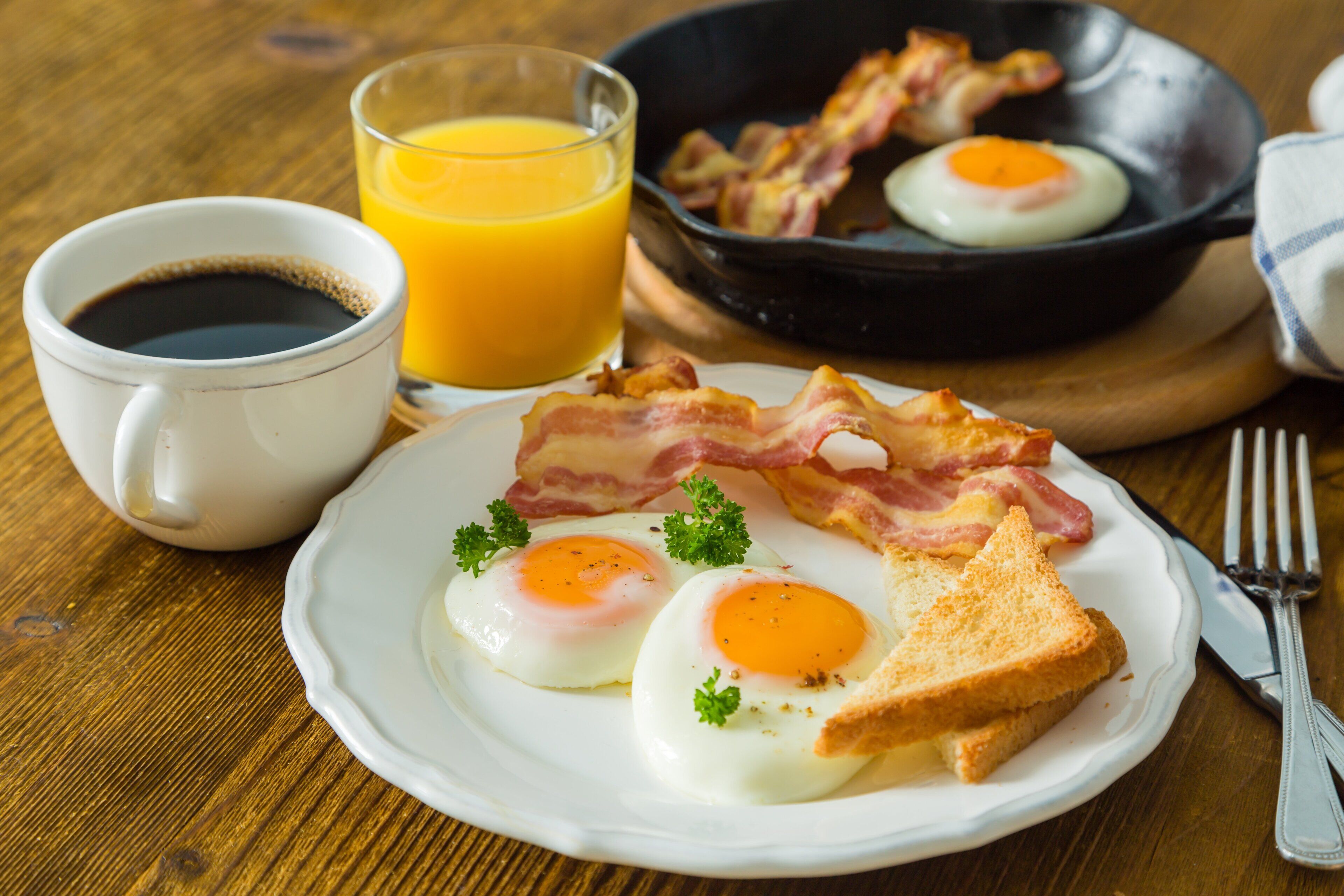 Une assiette de petit-déjeuner avec des œufs, du bacon, des toasts et une tasse de café accompagnée d’un jus d’orange.